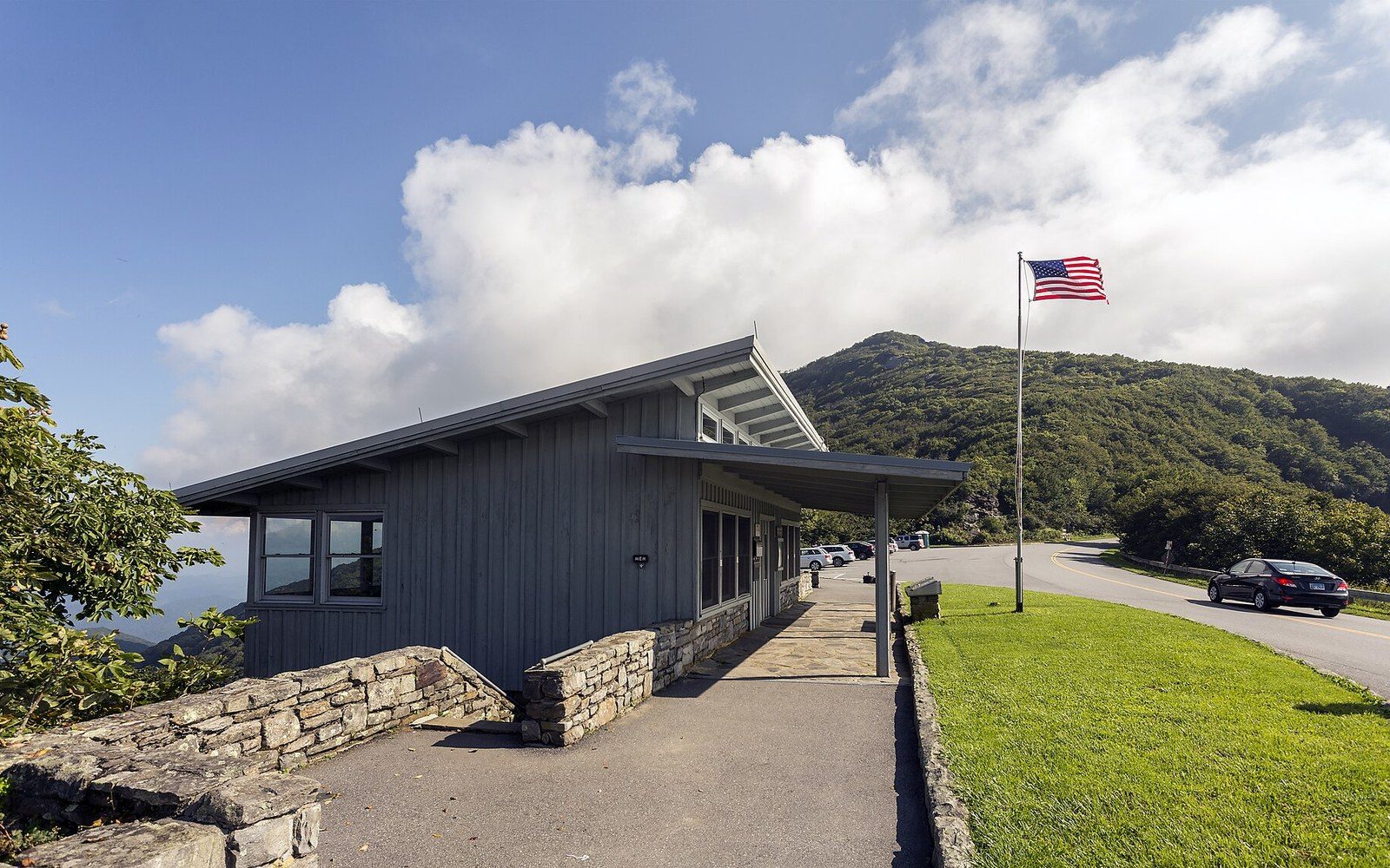 A wooden visitor center with an American flag near a mountain ridge