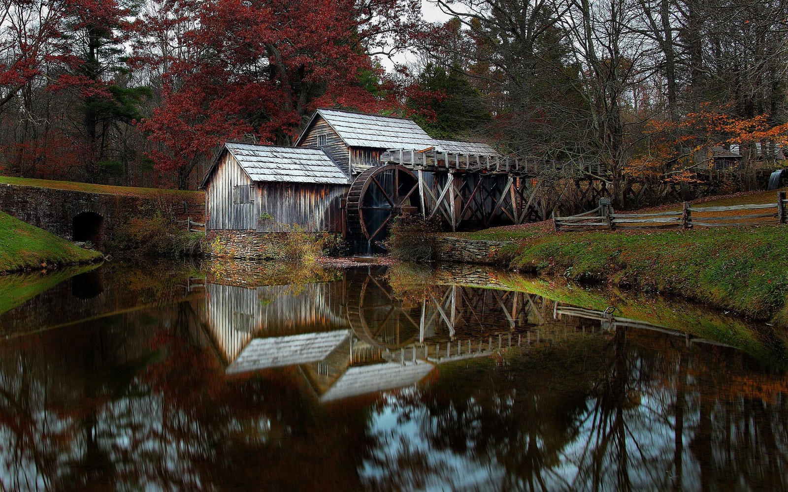 Wooden mill with waterwheel beside a pond, surrounded by autumn trees and their reflections