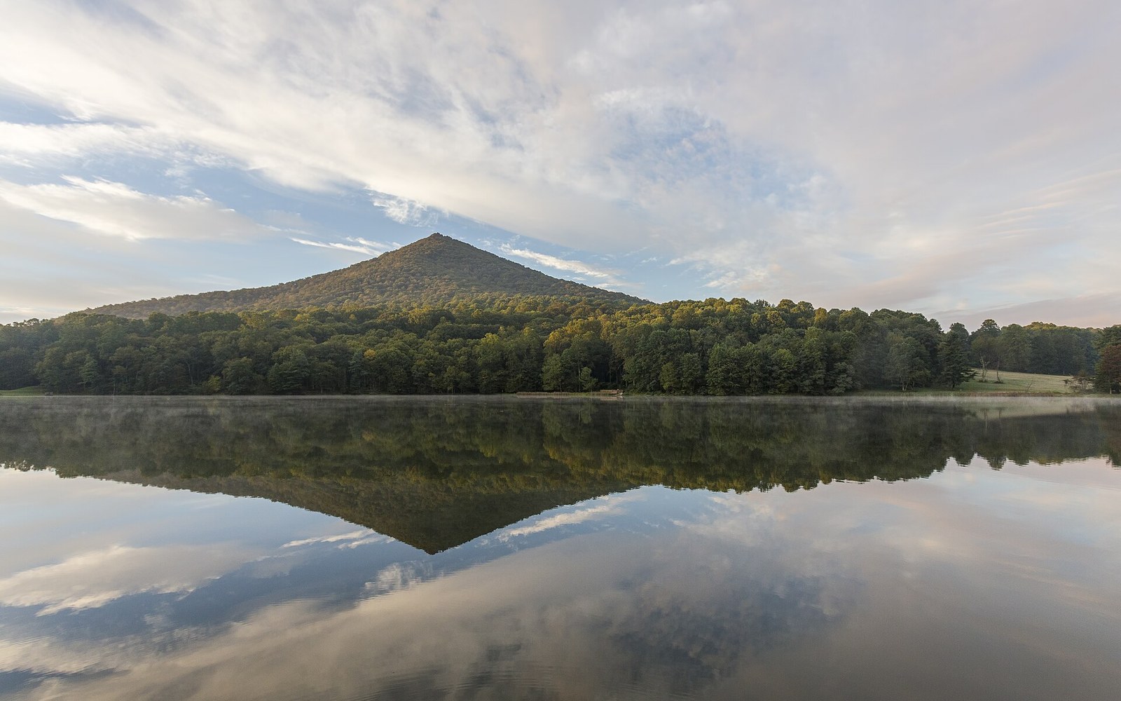 A conical mountain peak reflected in a still lake beneath a partly cloudy sky