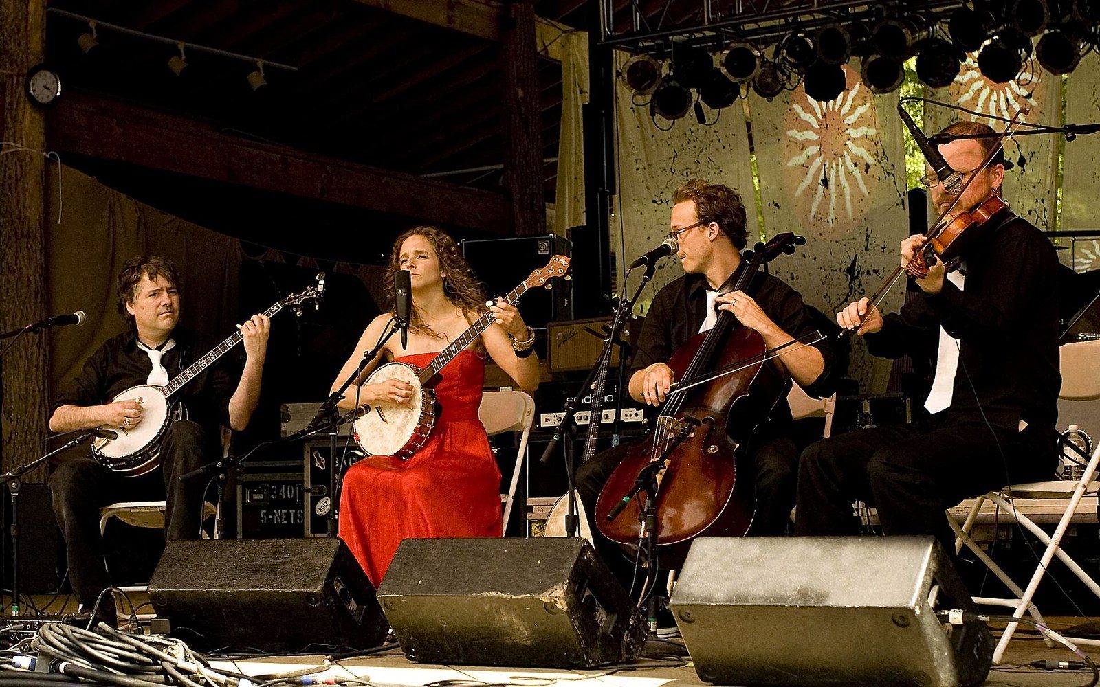 A four-piece string band performs on an outdoor stage with banjos, cello and fiddle
