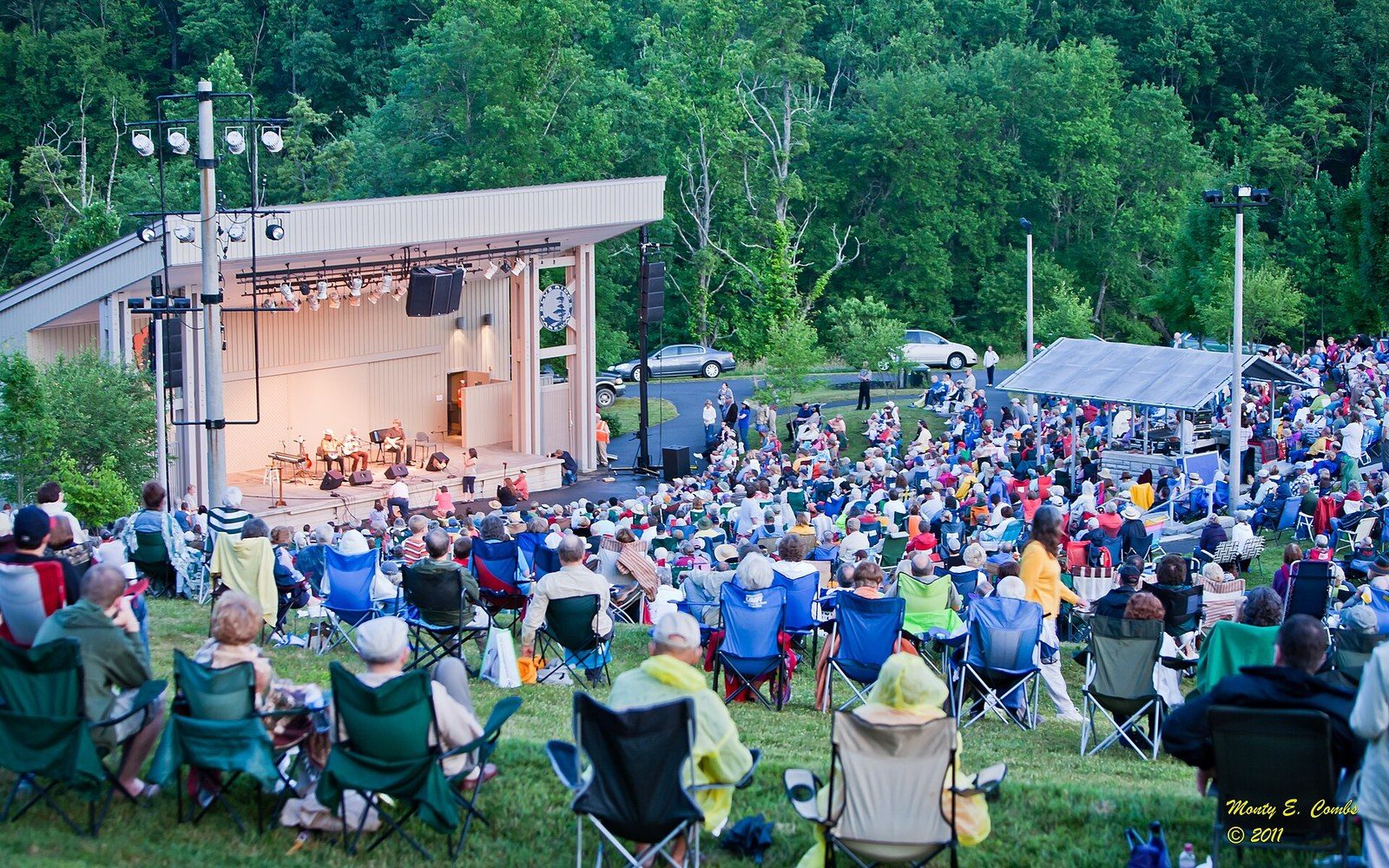 Crowd sits in lawn chairs facing an outdoor stage at the Blue Ridge Music Center