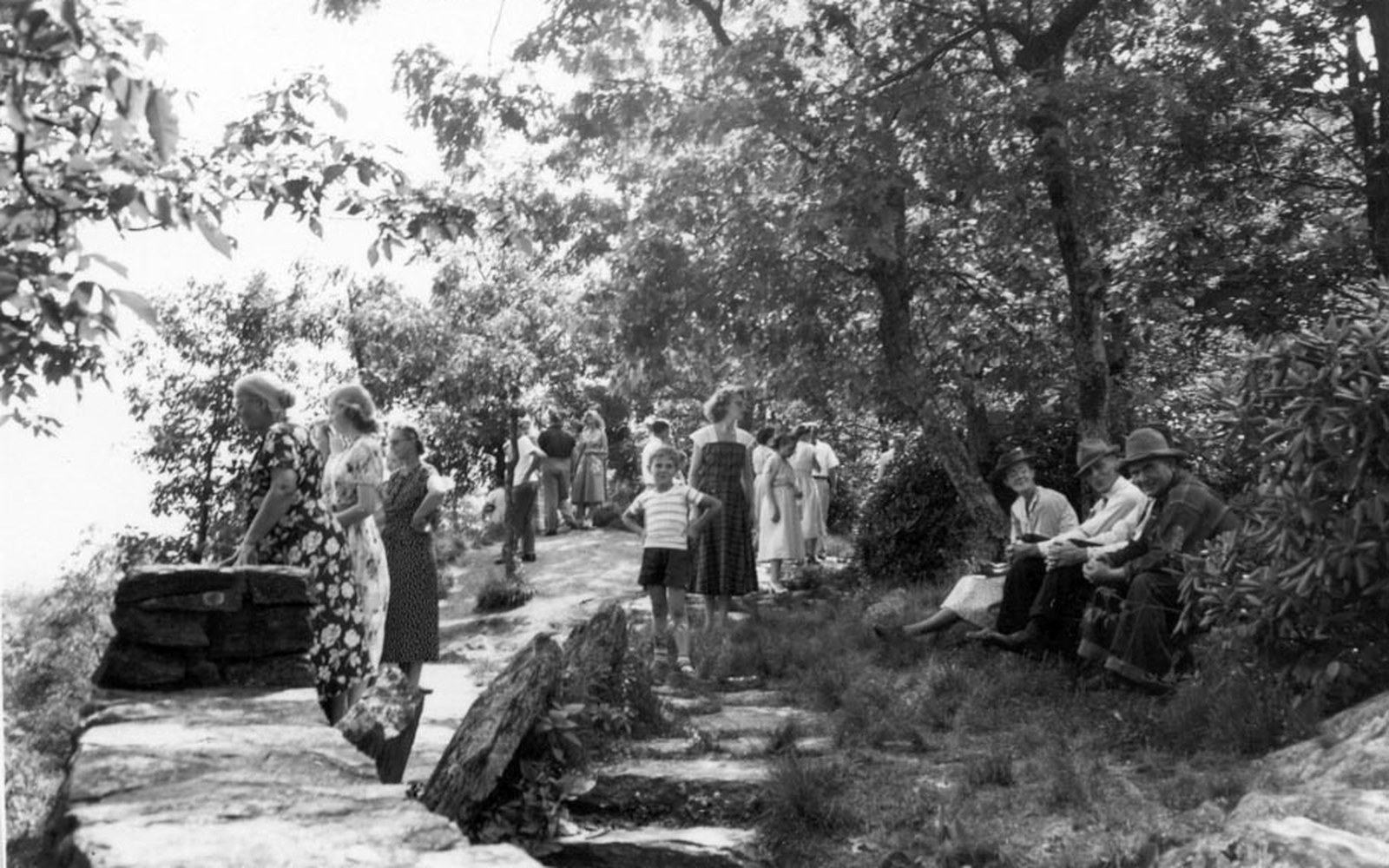 Group of people in vintage dress gather on a wooded overlook trail