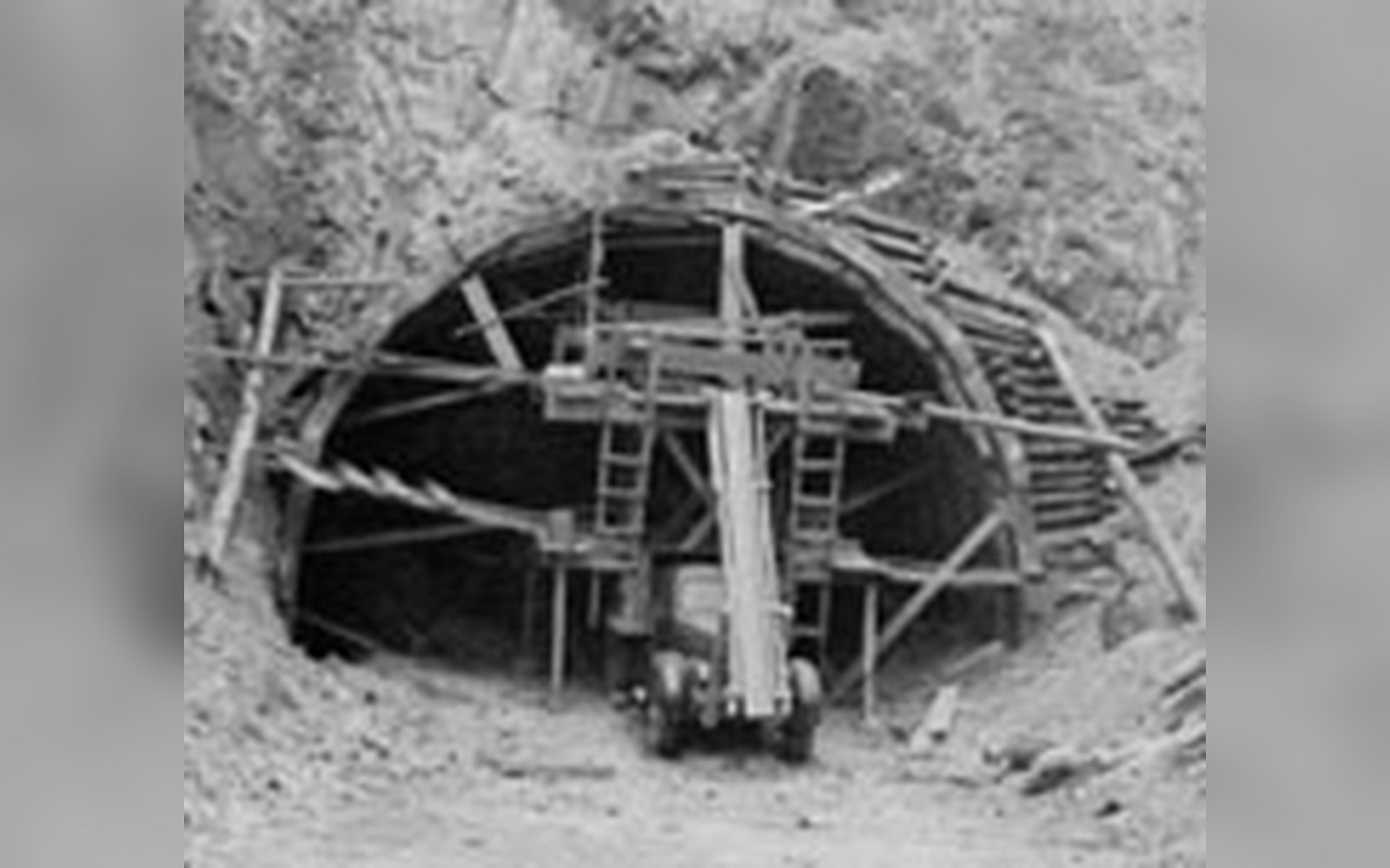 Wooden scaffolding and timber supports frame a mountain tunnel entrance under construction